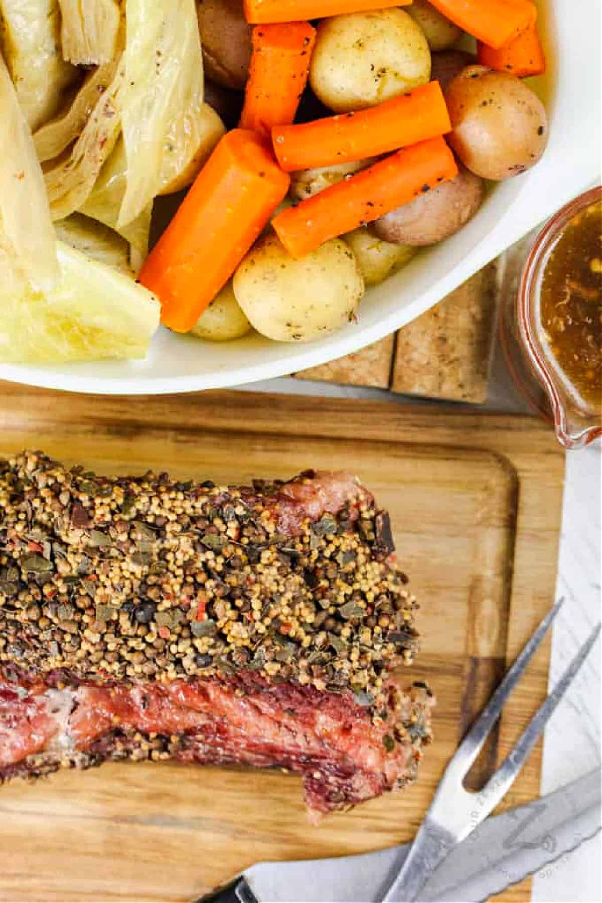 top view of Instant Pot corned beef and cabbage on a wooden platter, with carving utensils on the side, with a side of cabbage, potatoes, carrots and gravy