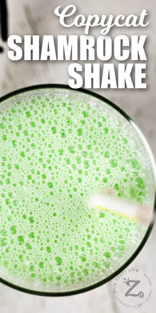 copycat shamrock shake in a clear glass with a straw and a towel beside it, with writing