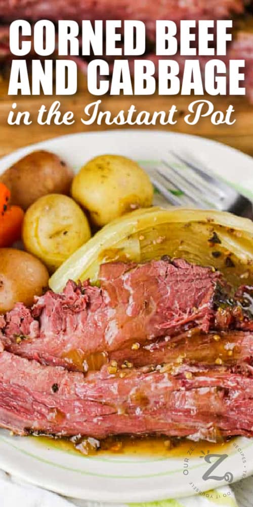 Instant Pot corned beef and cabbage, potatoes and carrots served on a white plate, with sliced corned beef in the background, with a title