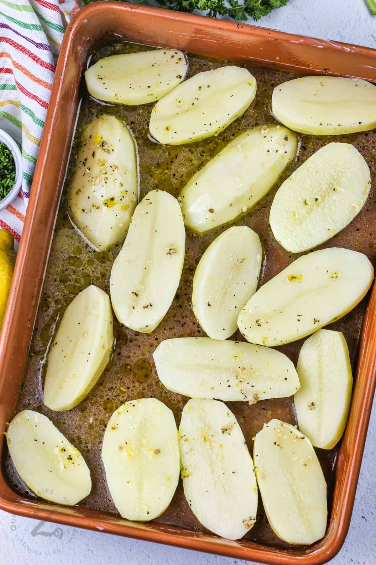 potatoes in a casserole dish with dressing to make Greek Style Lemon Potatoes