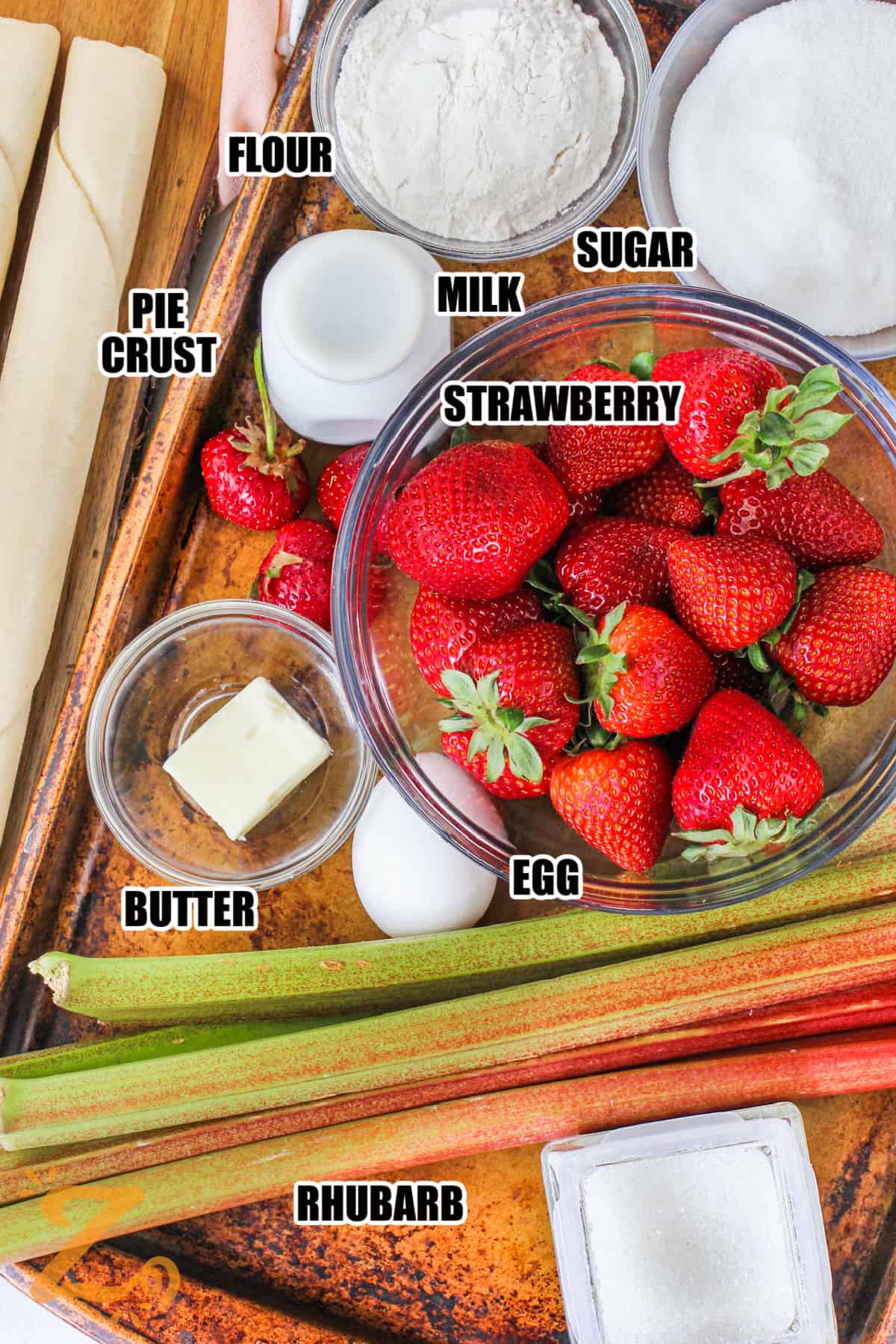 flour , sugar , milk , pie crust , strawberries , butter , egg and rhubarb with labels to make Strawberry Rhubarb Pie