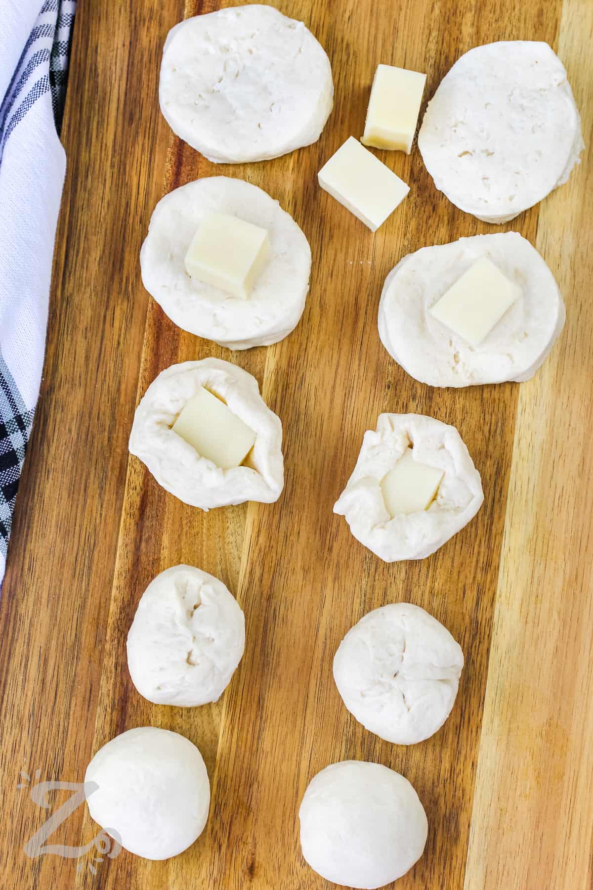 biscuits on a cutting board showing the steps to wrap them around cheese cubes.
