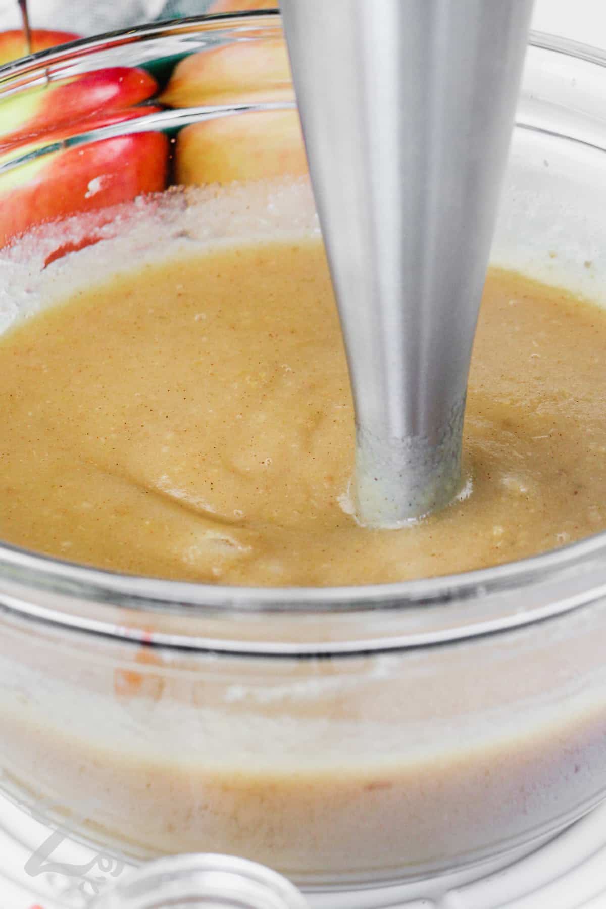 Mashed apples being pureed with an immersion blender to make homemade apple sauce