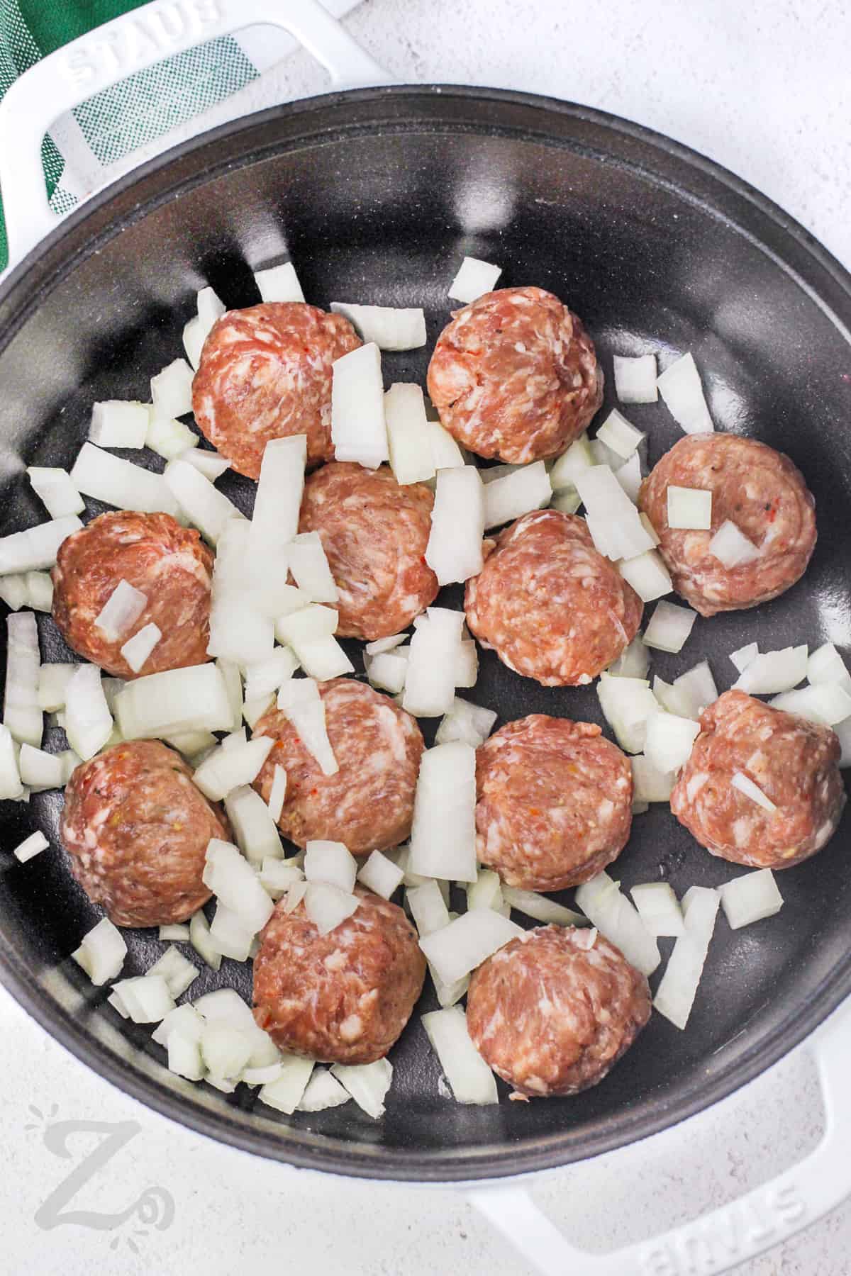 uncooked meatballs and onions in a frying pan