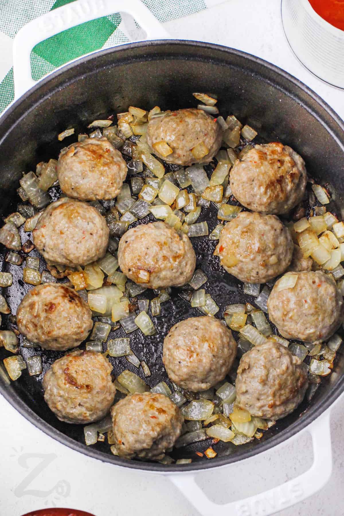 meatballs being cooked in a frying pan with onions