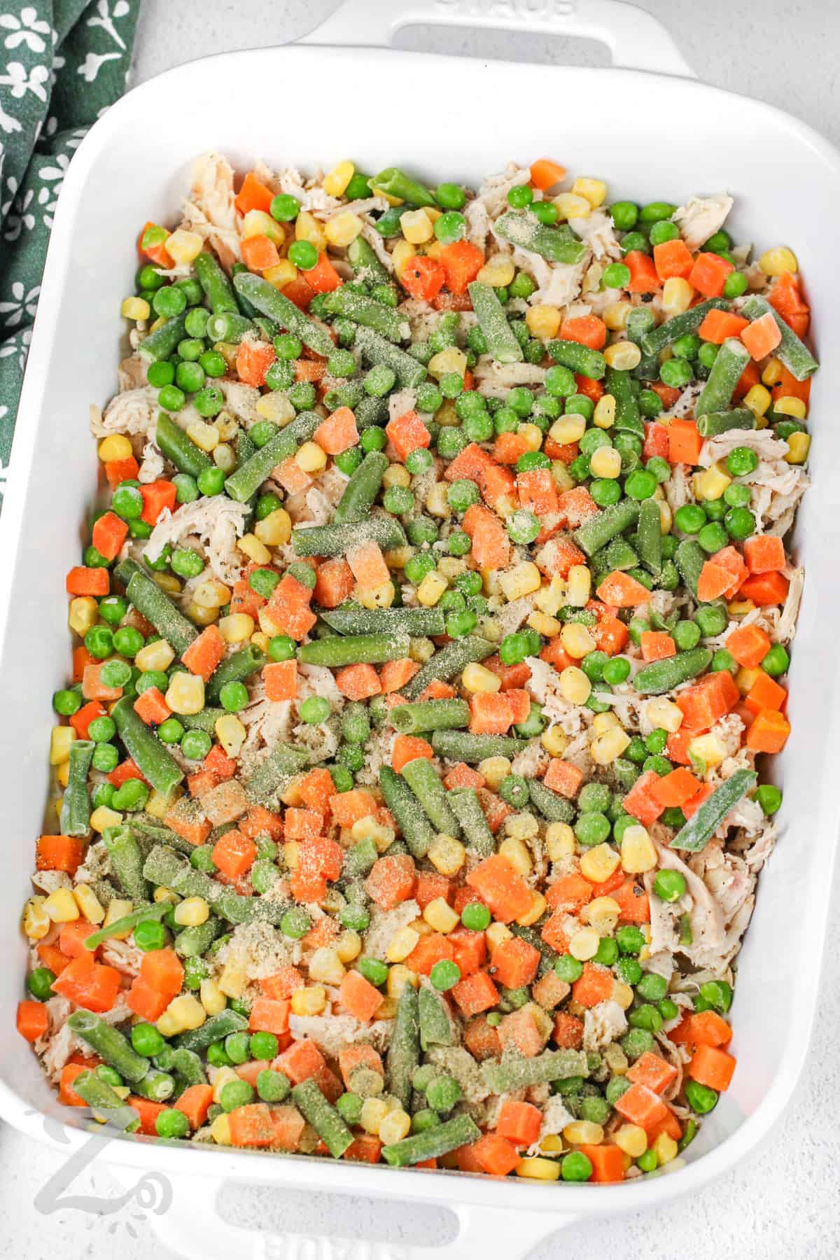 frozen veggies spread over shredded chicken in a casserole dish