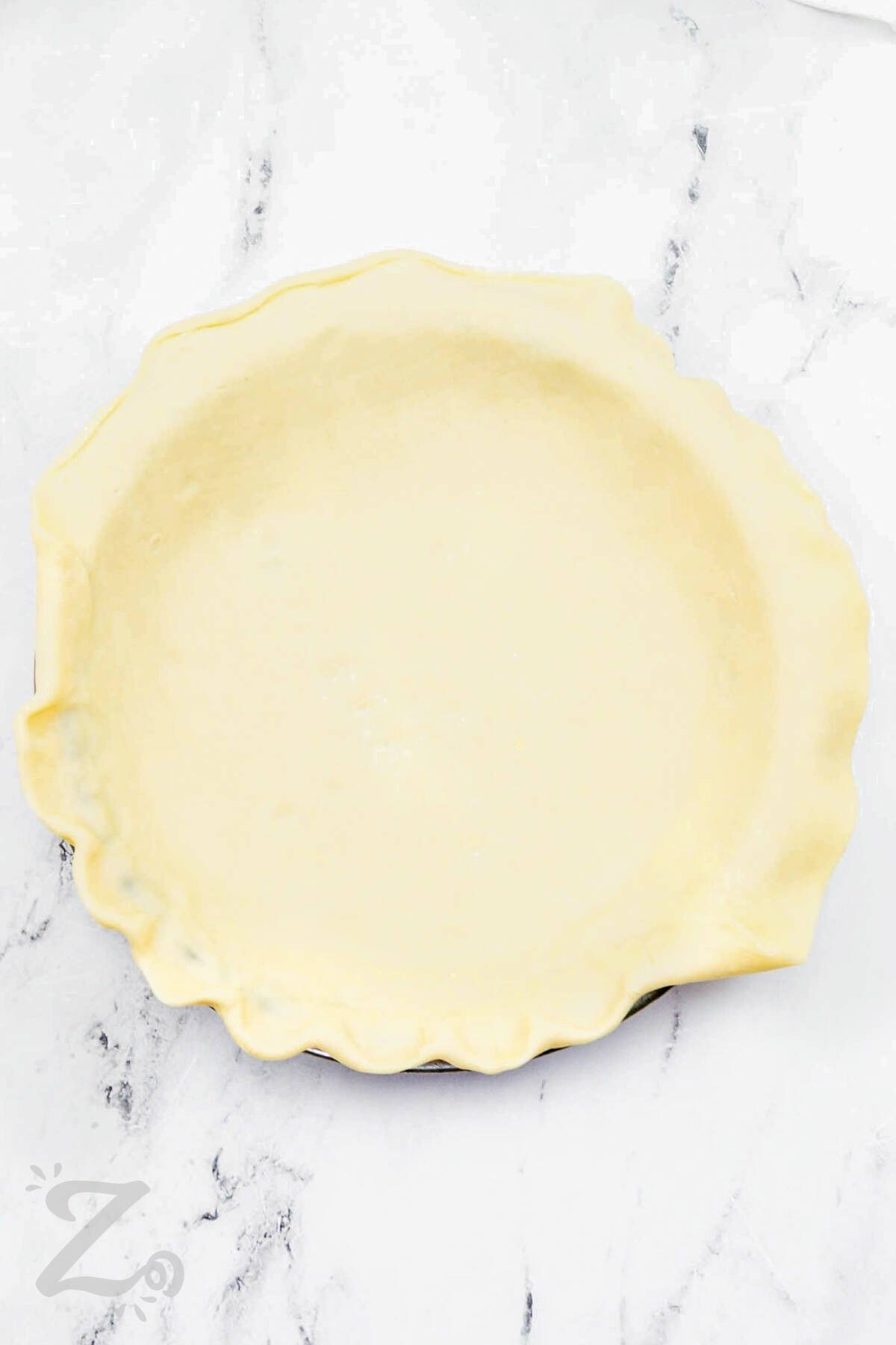 pie crust in a pie plate with the edges being crimped