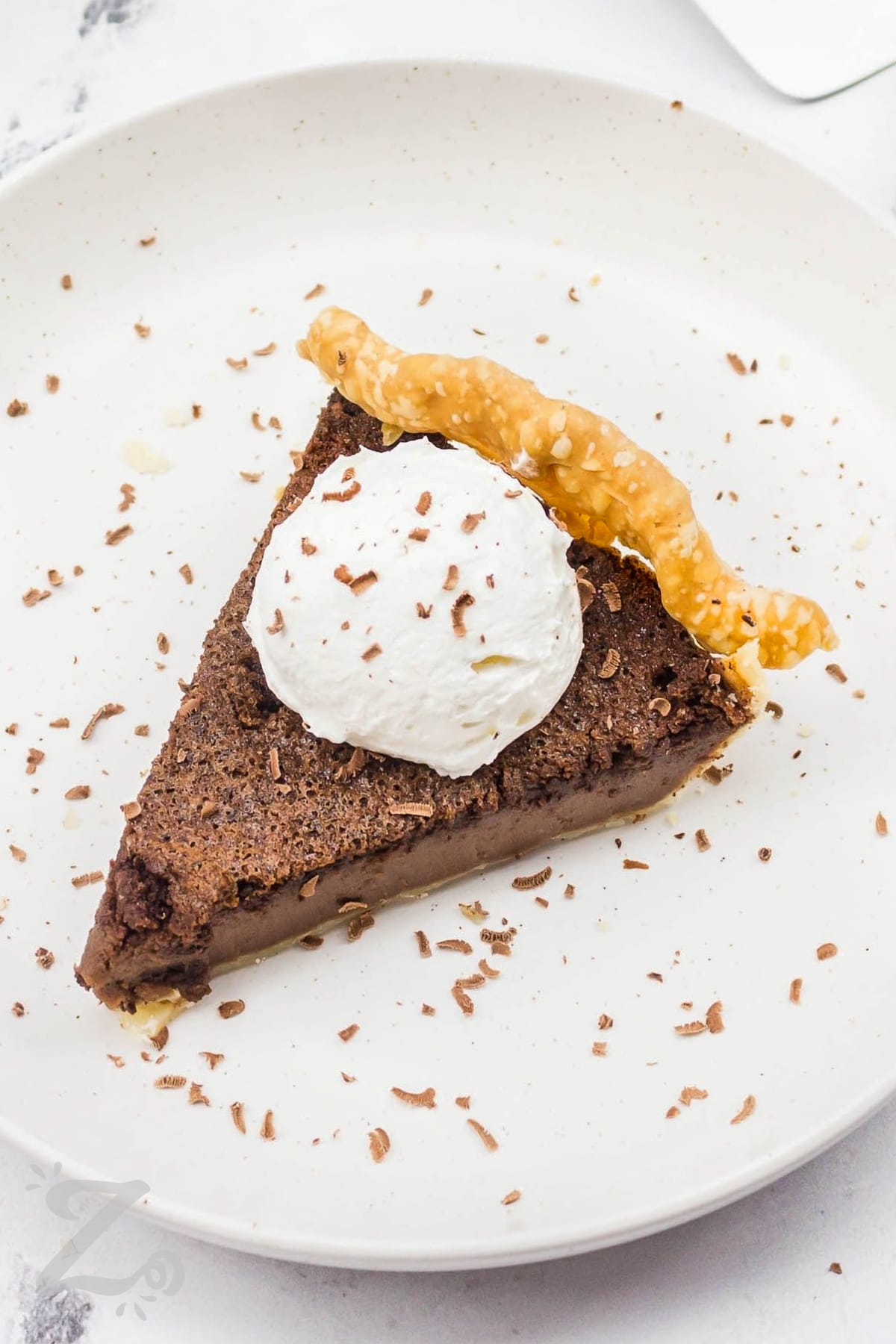 A slice of chocolate chess pie topped with whipped cream and chocolate shavings
