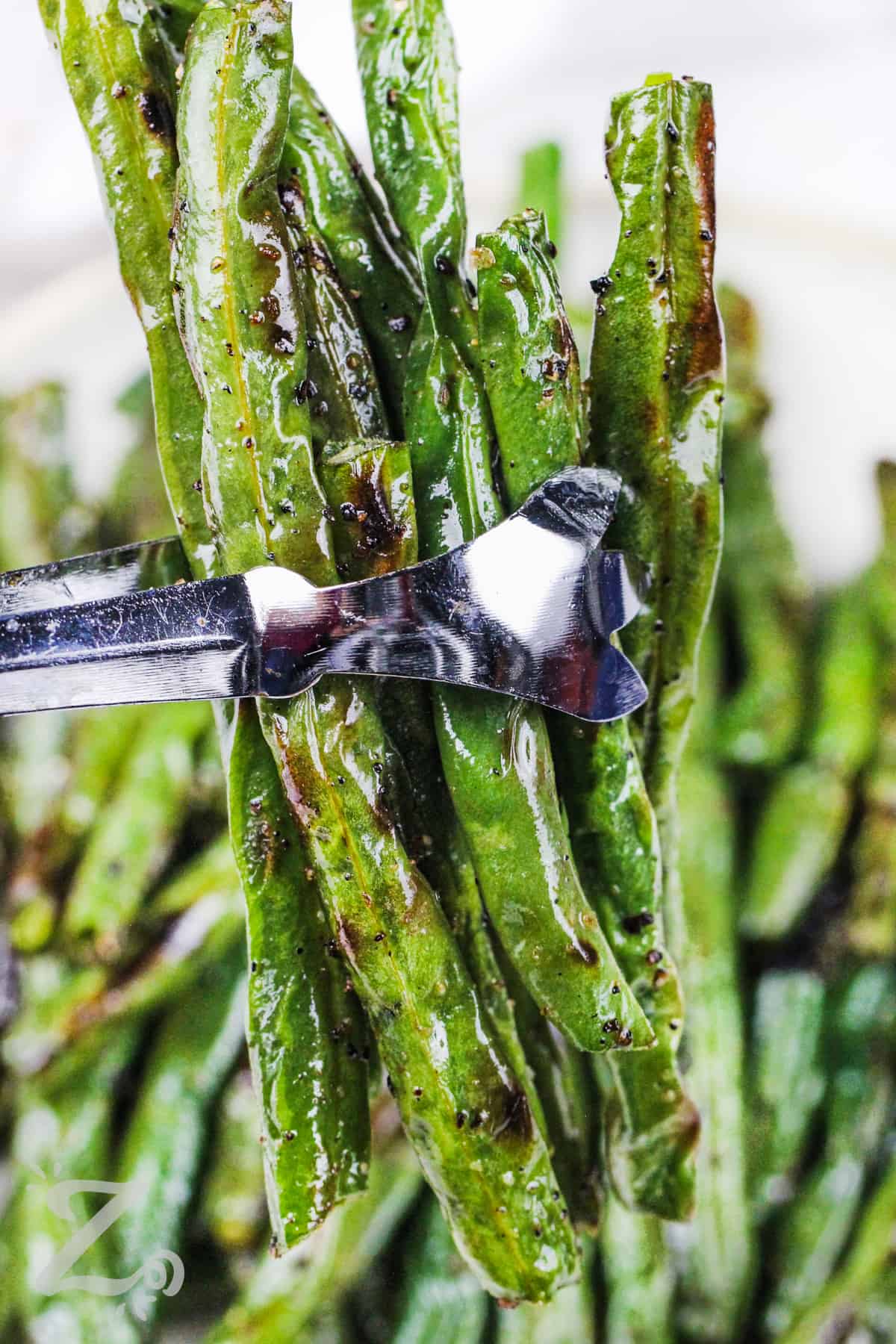 grilled green beans being held up by tongs