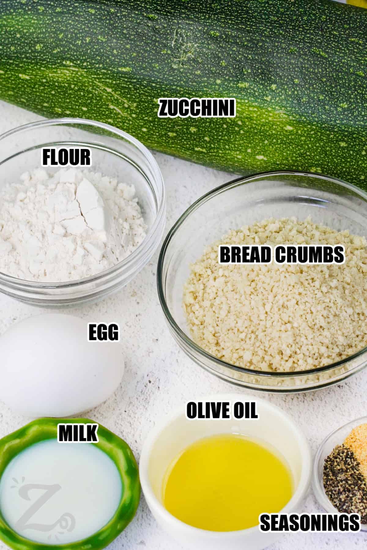 ingredients to make zucchini sticks labeled: zucchini, flour, bread crumbs, egg, milk, oilive oil and seasonings