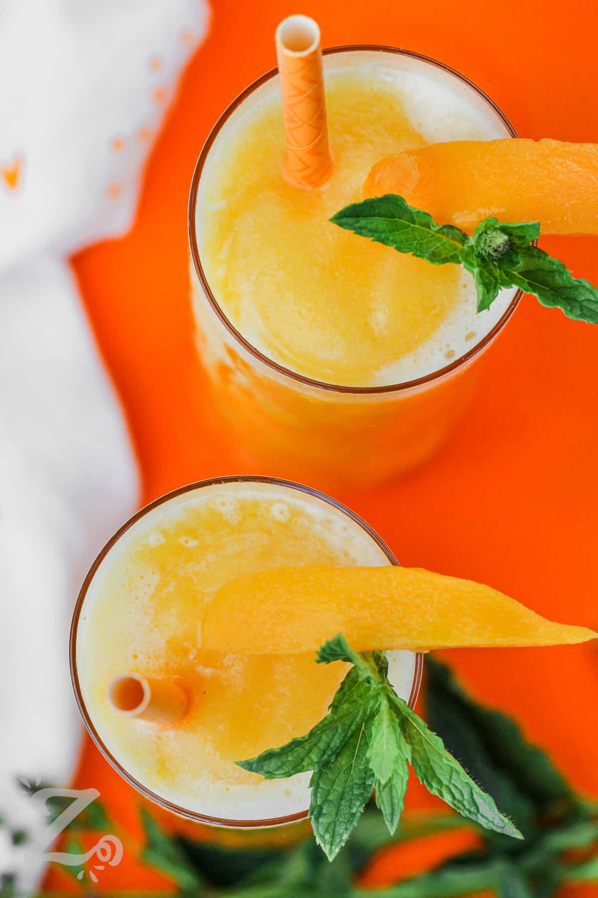Top view of two peach bellini's topped with peach slices and mint leaves with a straw