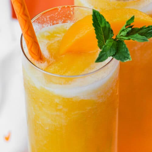 peach bellini topped with peach slices and mint leaves with a straw