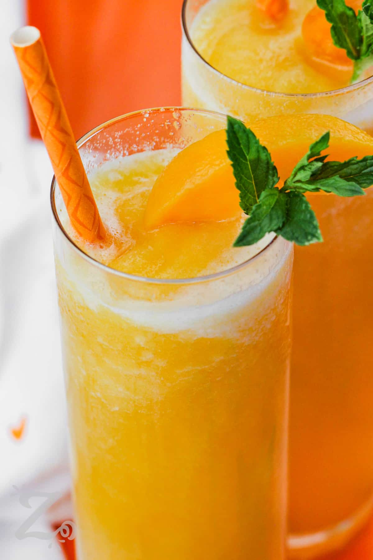 peach bellini topped with peach slices and mint leaves with a straw