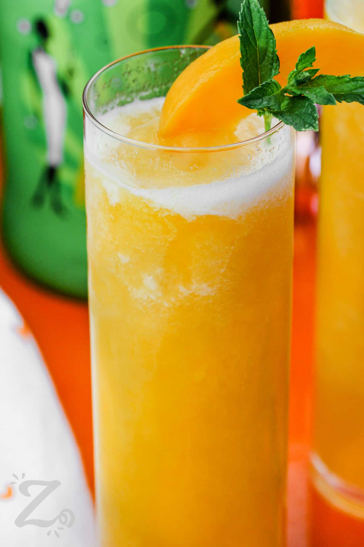 a peach bellini topped with a peach slice and mint leaves