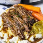 slow cooker Mississippi pot roast on a plate of mashed potatoes with gravy and carrots
