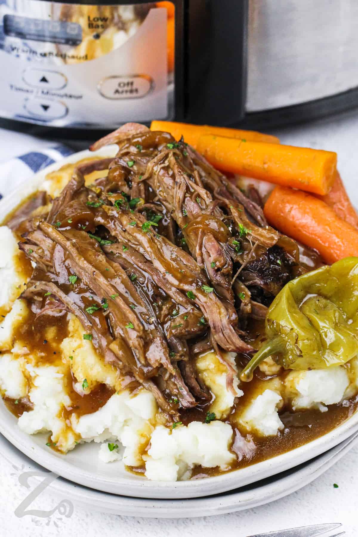 slow cooker Mississippi pot roast on a plate of mashed potatoes with gravy and carrots