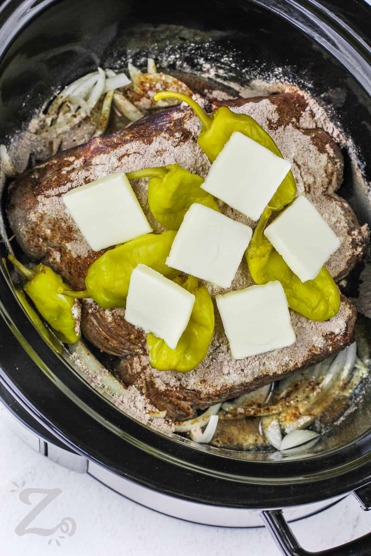 pot roast in a crockpot with peppers and squares of butter for slow cooker Mississippi pot roast