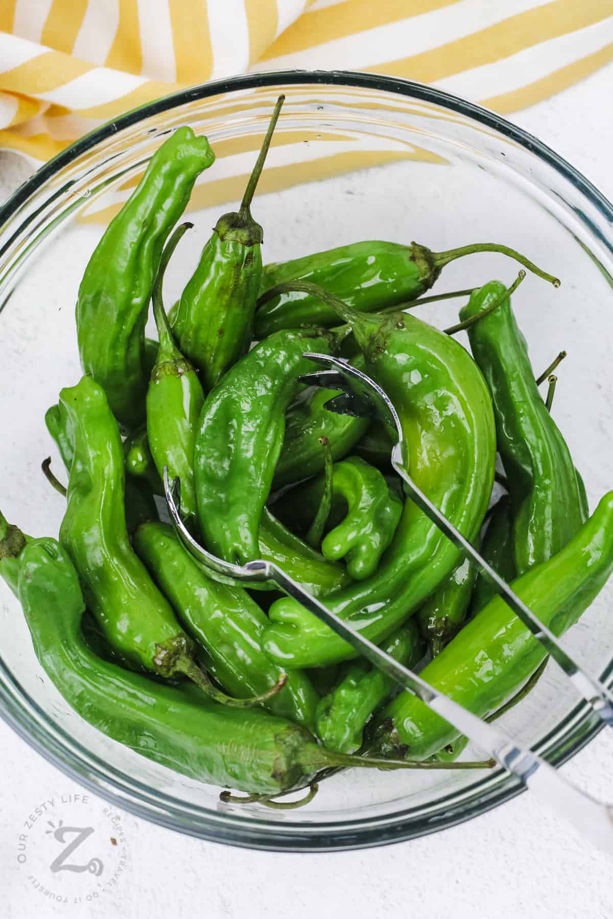 shishito peppers in a glass bowl with tongs