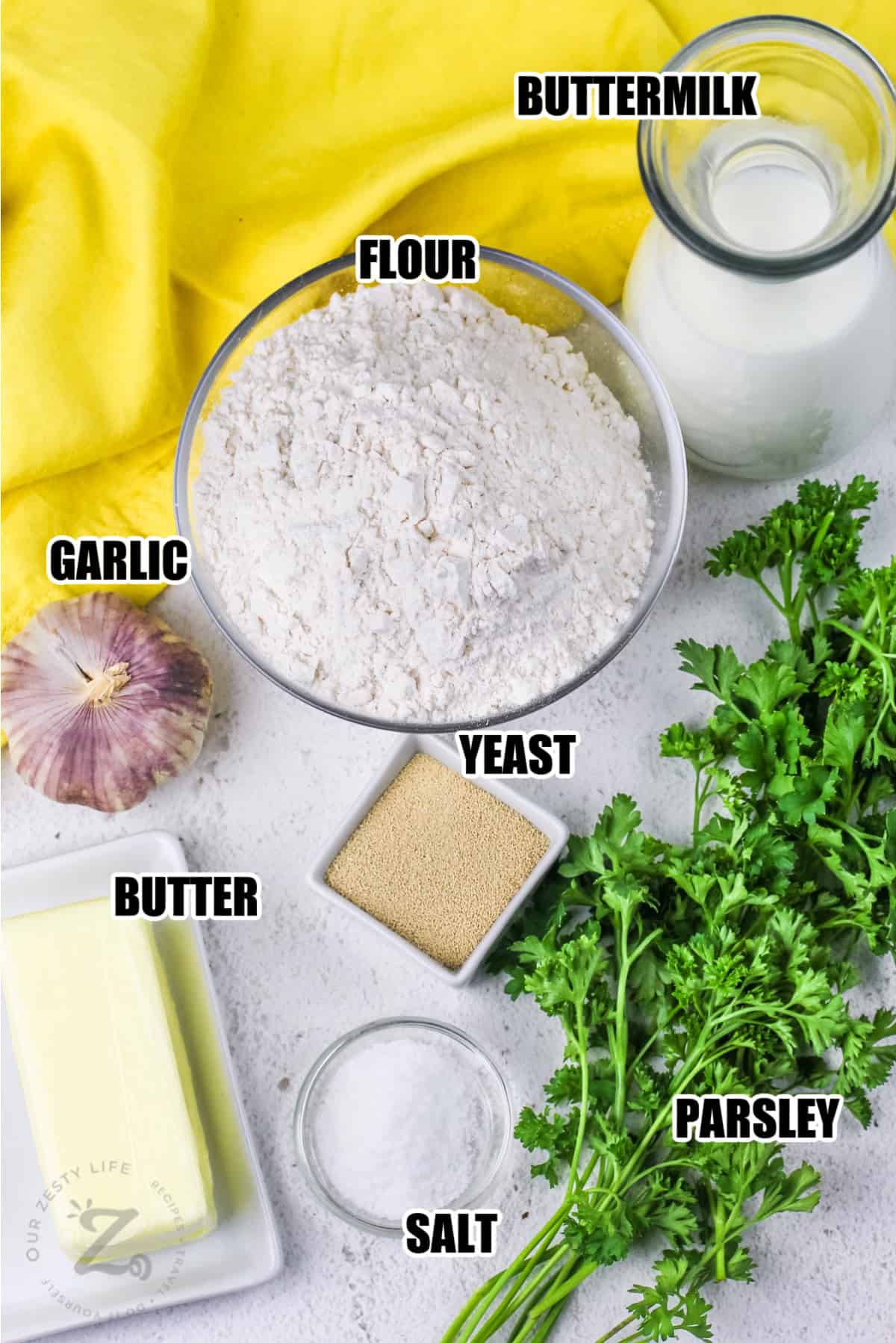 ingredients to make garlic herb bread including buttermilk, flour, garlic, yeast, butter, parsley, and salt