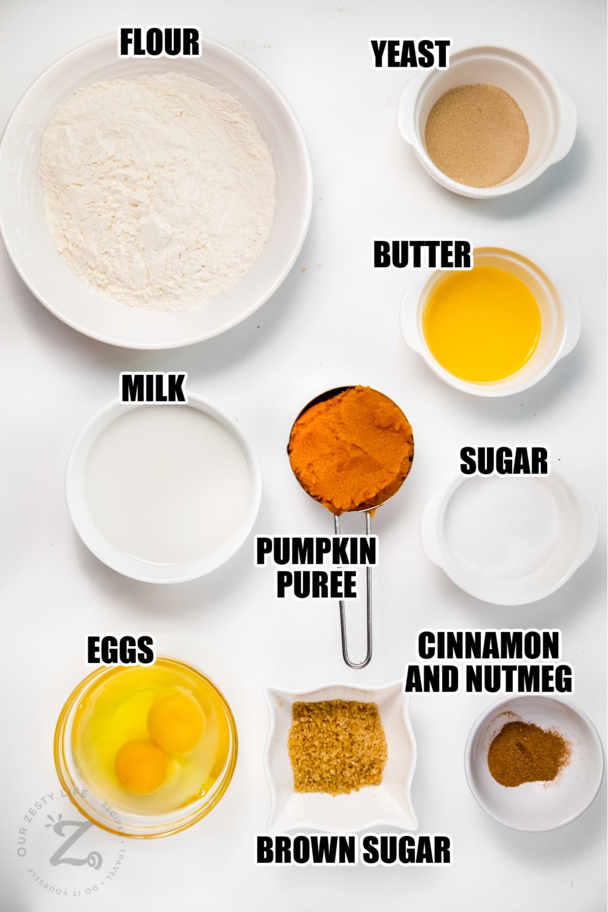ingredients to make pumpkin cinnamon rolls including flour, yeast, butter, milk, sugar, pumpkin puree, cinnamon, nutmeg, eggs, and brown sugar