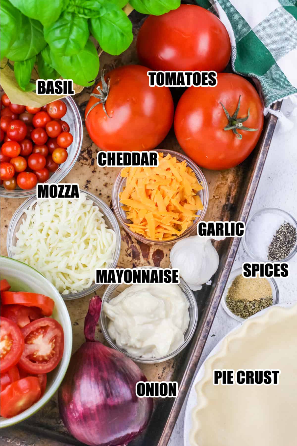 ingredients to make tomato pie including basil, tomatoes, cheddar, mozza, mayonnaise, garlic, spices, onion, and pie crust