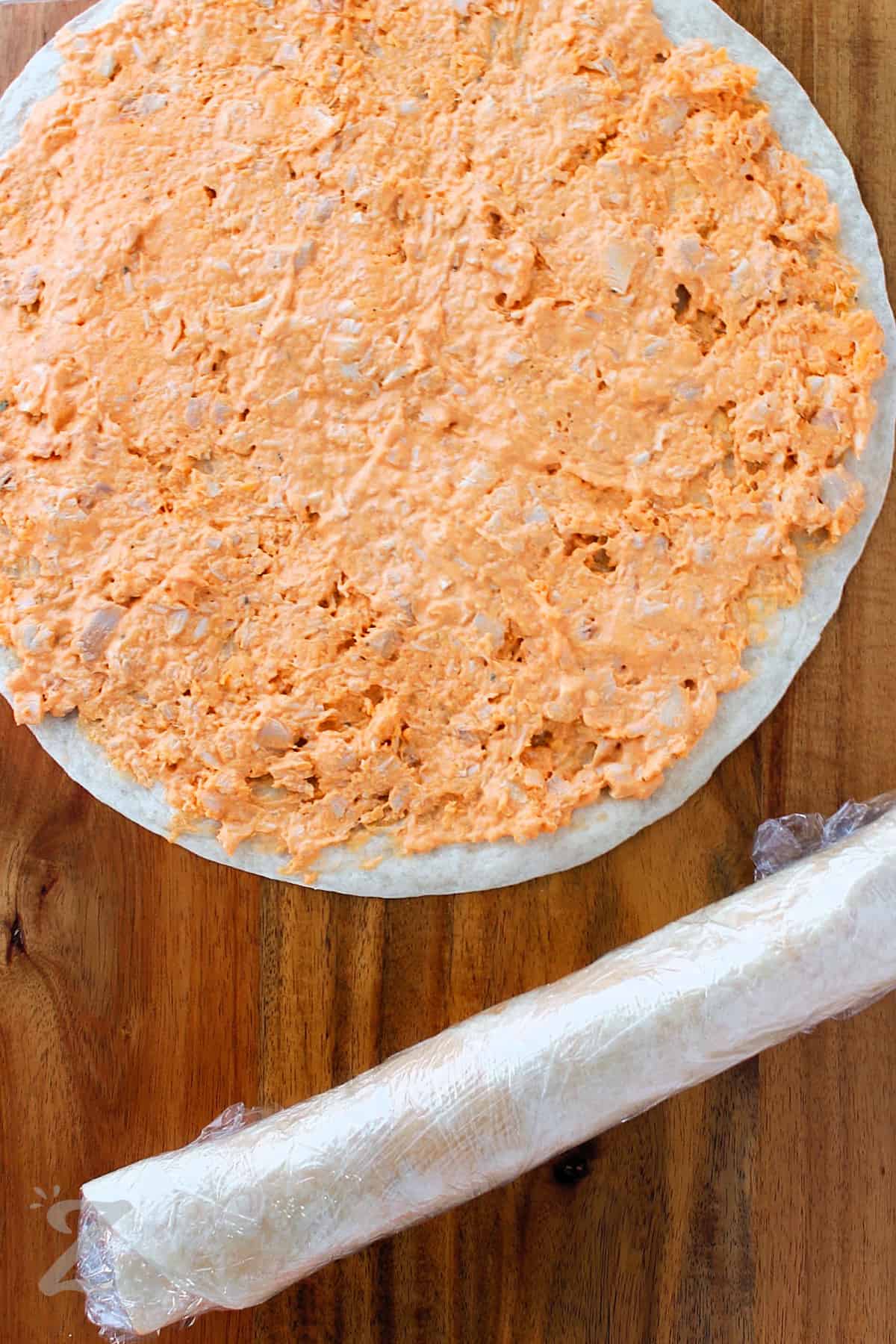adding filling to tortilla and rolling it up to make Buffalo Chicken Pinwheels