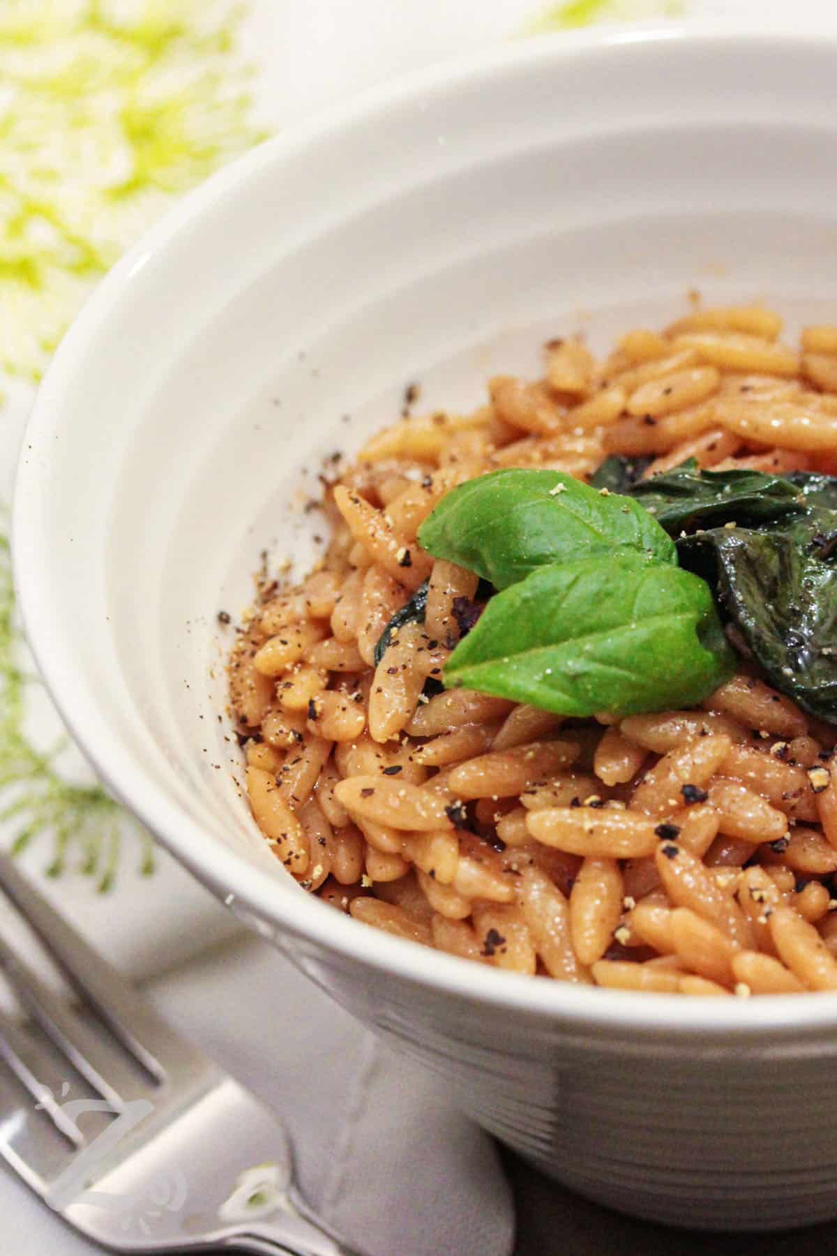 parmesan orzo with basil in a white bowl, garnished with basil leaves