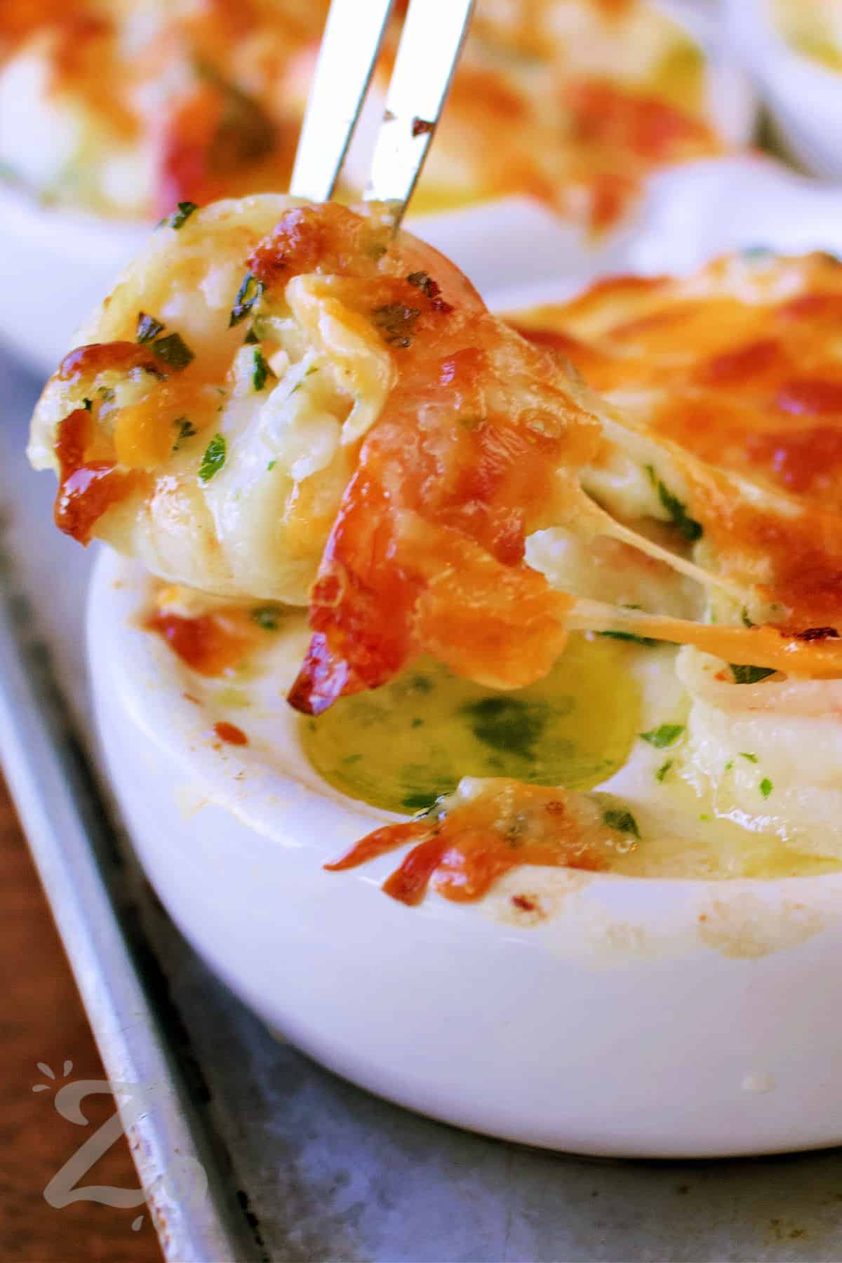a cheesy garlic baked shrimp being pulled with a shrimp fork from an escargot dish