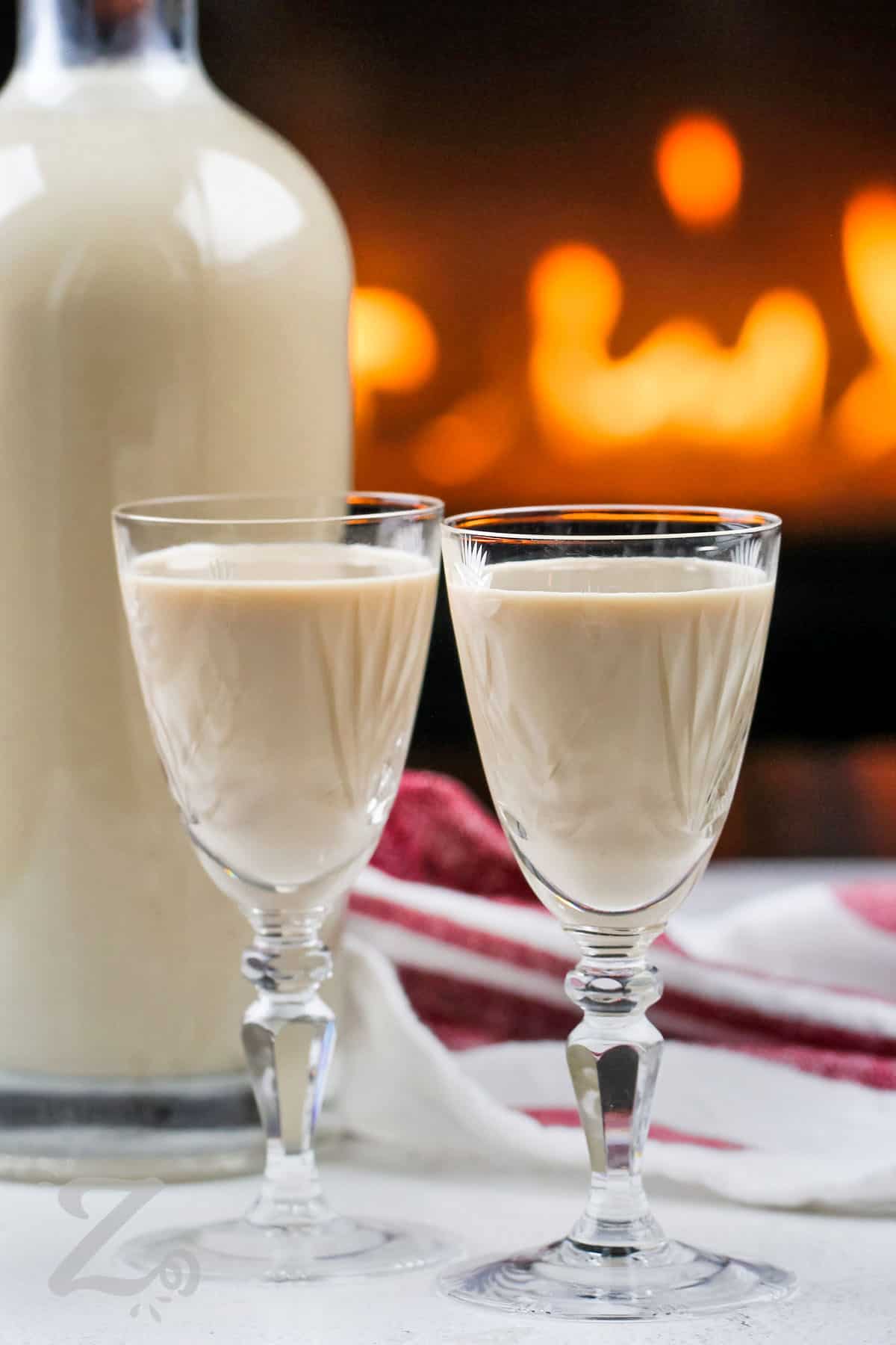 Two glassed of homemade Irish cream with a bottle in the background