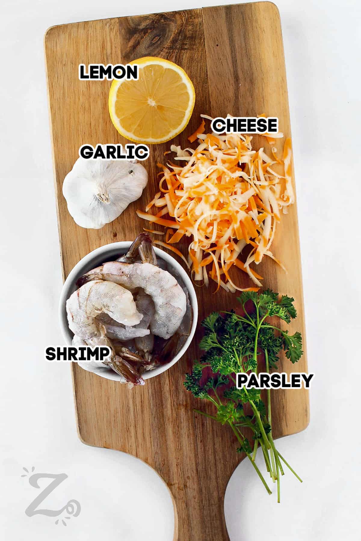 lemon, shredded cheese, garlic, fresh parsley and shrimp, assembled on a wooden board, ready to make cheesy garlic baked shrimp