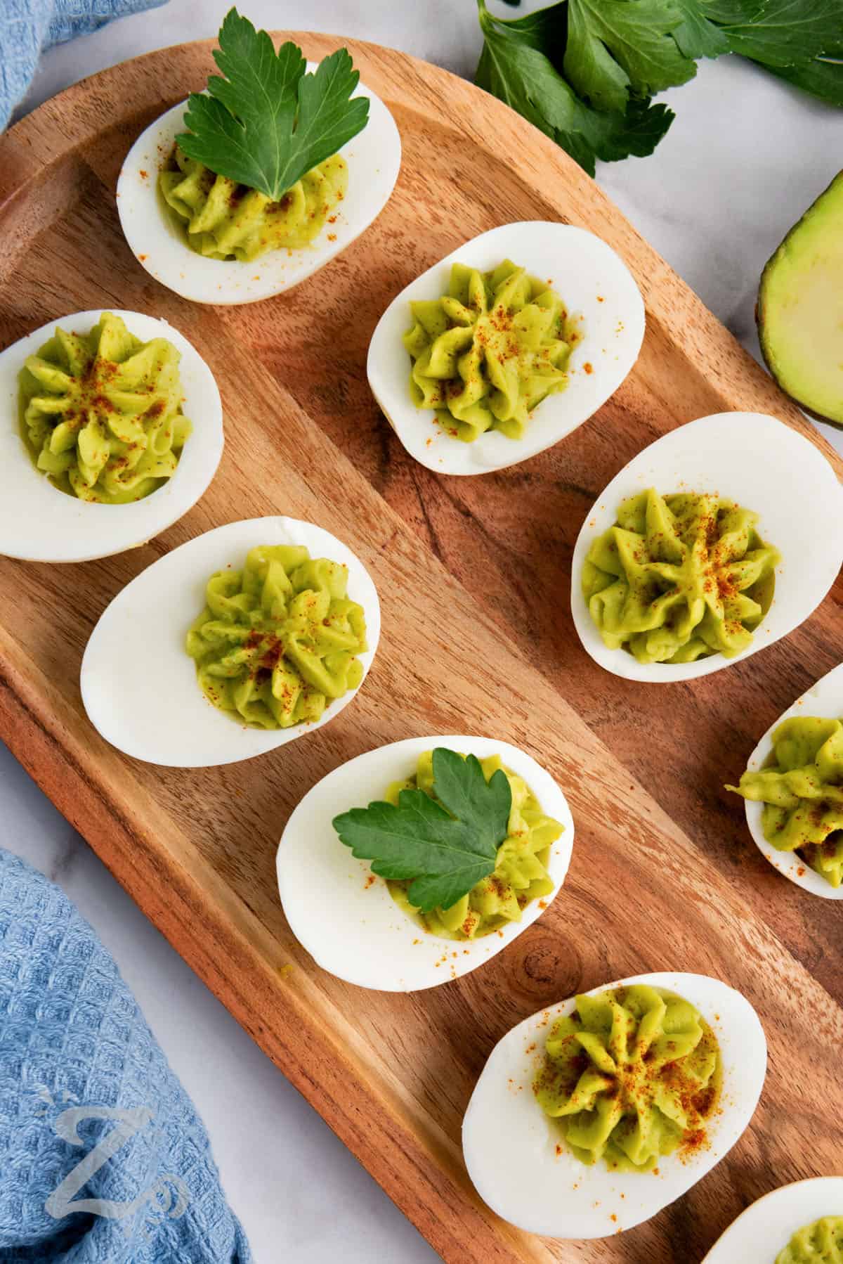 avocado deviled eggs topped with parsley on a serving board