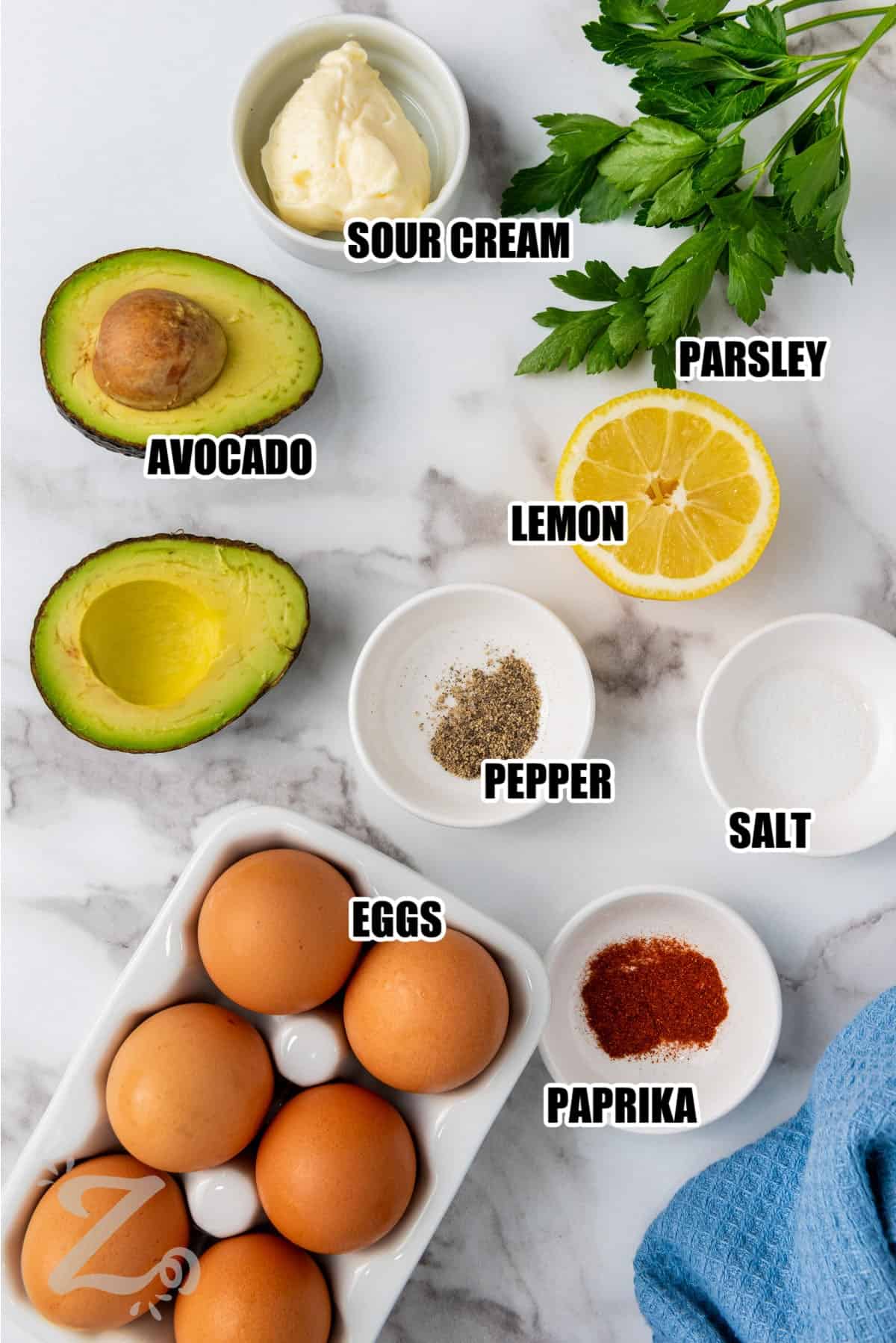 avocado, sour cream, lemon, eggs, salt and pepper, paprika and parsley assembled to make avocado deviled eggs