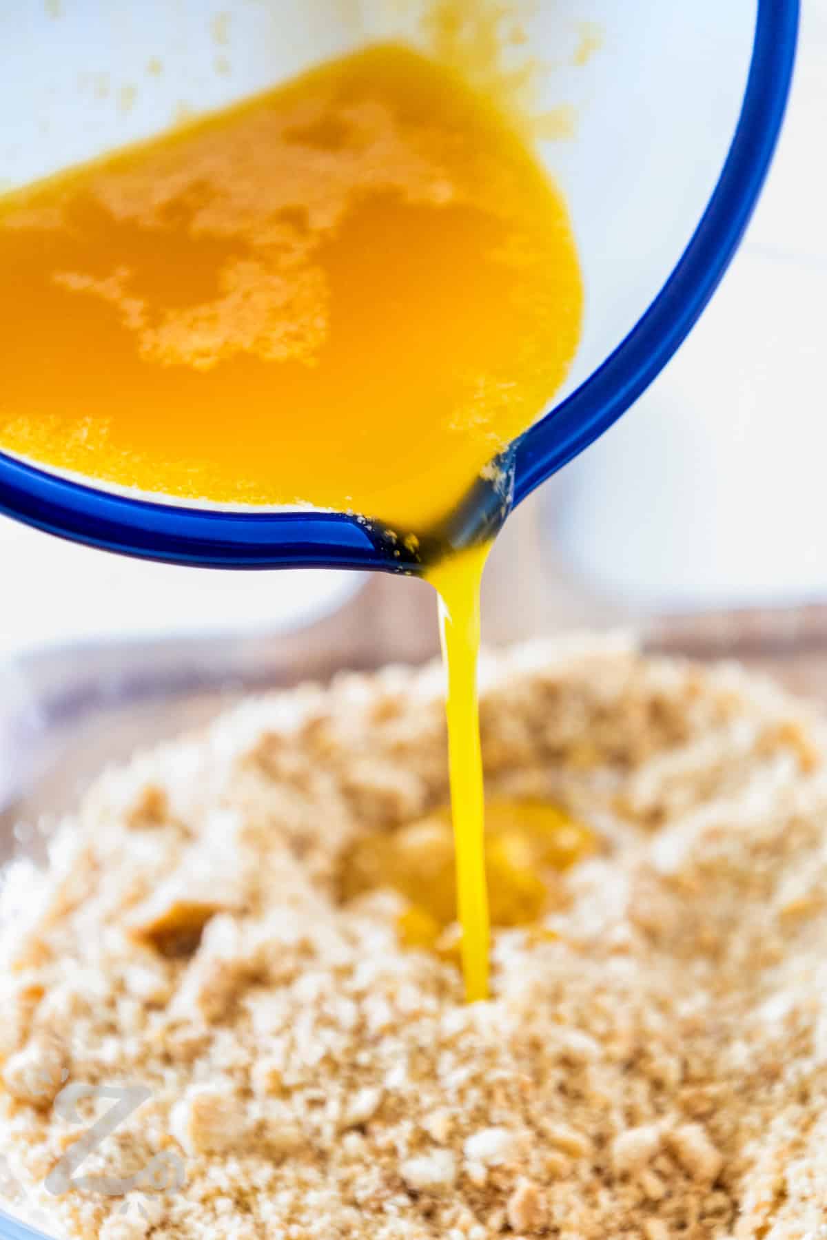 melted butter being added to the crushed crisp cookies used to make the crust for a No Bake Strawberry Cheesecake