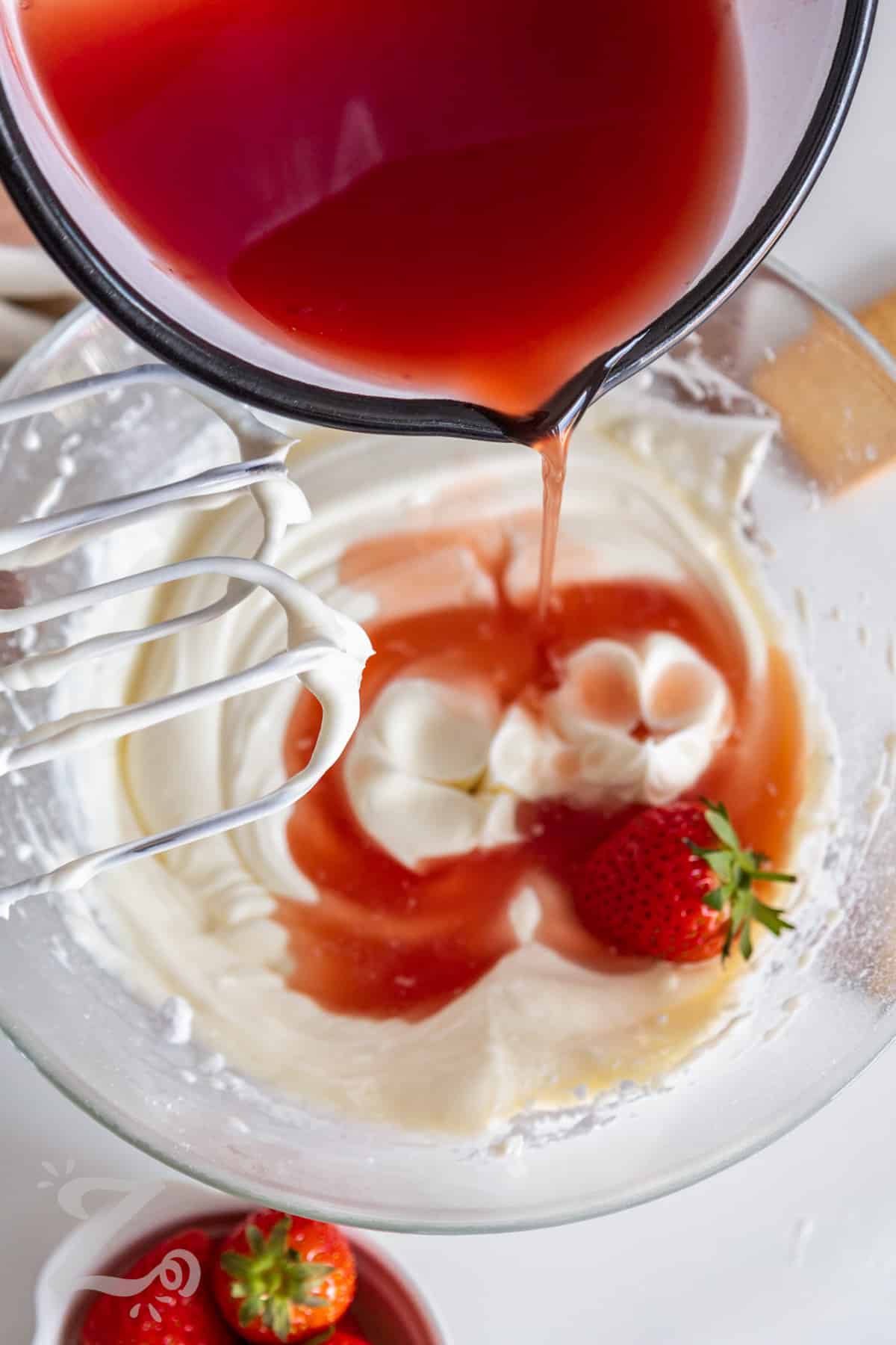 prepared strawberry gelatin being poured into the no bake strawberry cheesecake filling