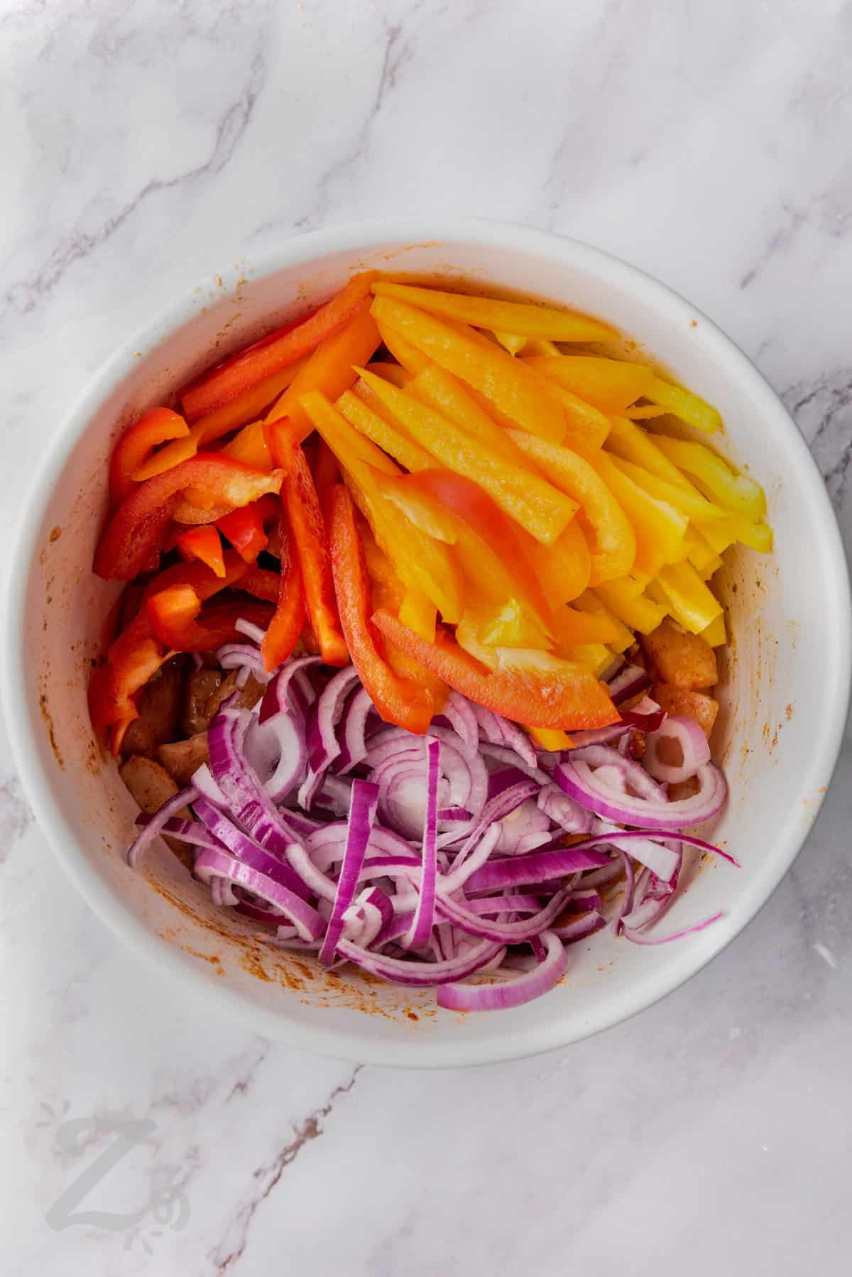 chicken breasts, bell peppers, and red onions in a bowl