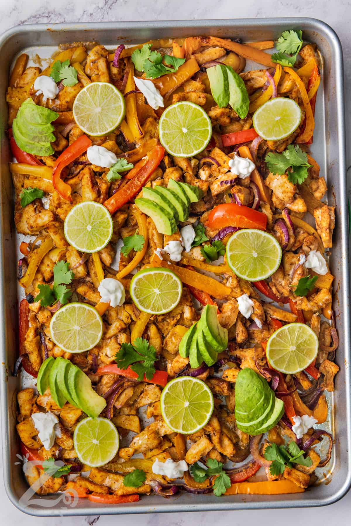 chicken fajita filling on a sheet pan topped with limes, avocados, and cilantro