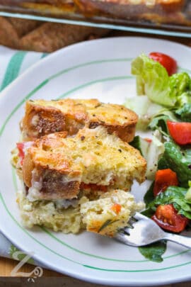 Breakfast strata with a fork full of strata on a plate with a tossed salad on the side