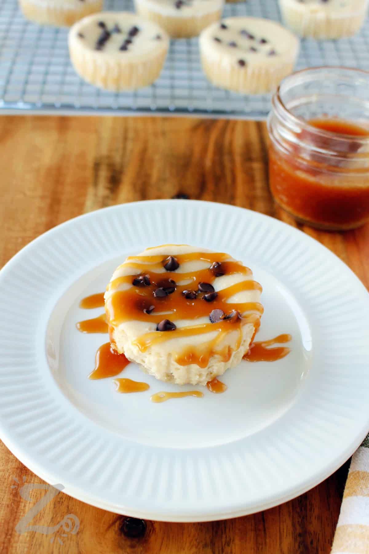 caramel poured over one of the caramel mini cheesecakes on a white plate.