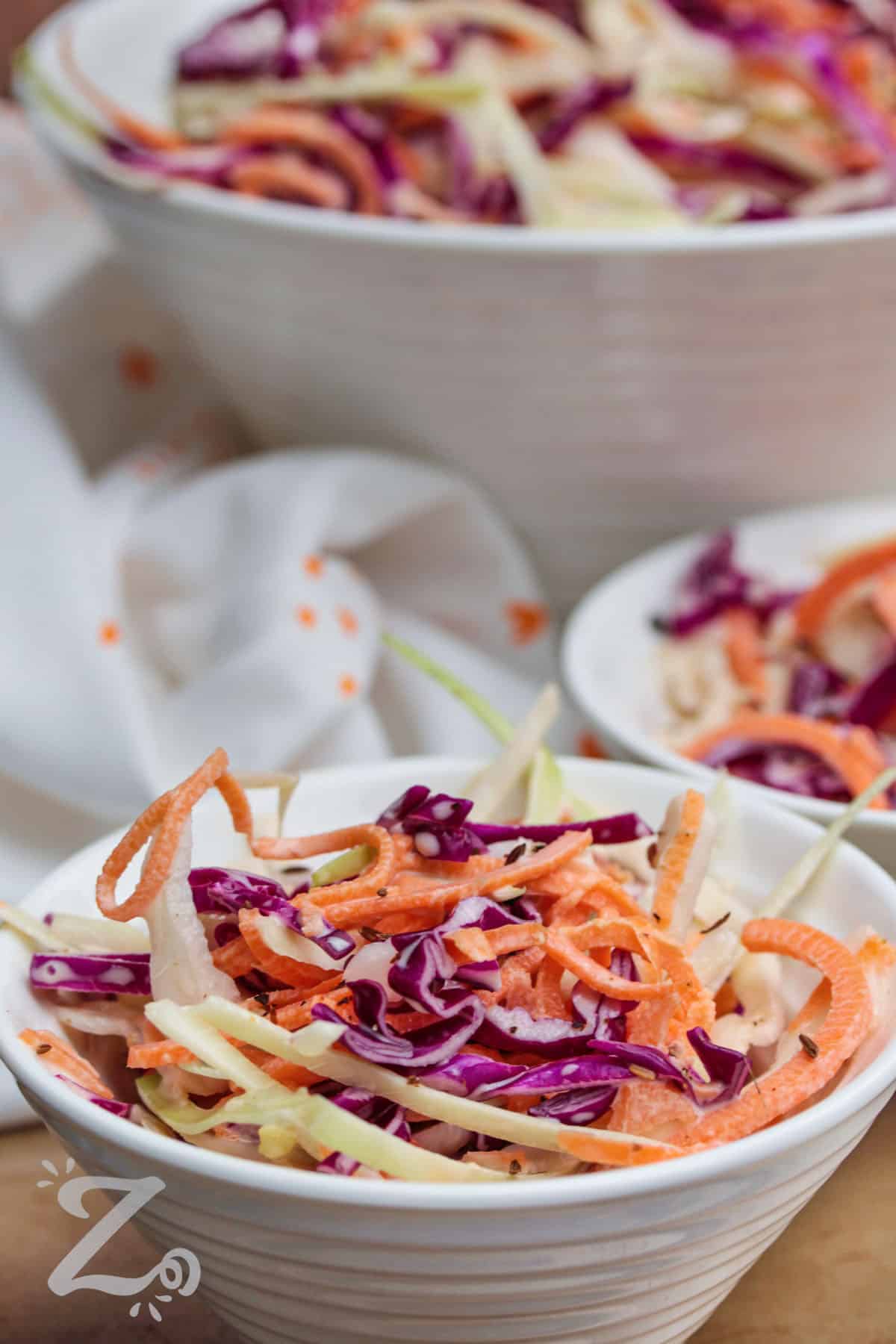 a serving of creamy coleslaw in a small bowl, with a large bowl of coleslaw in the background