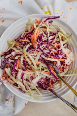 creamy coleslaw in a white bowl with silver tongs