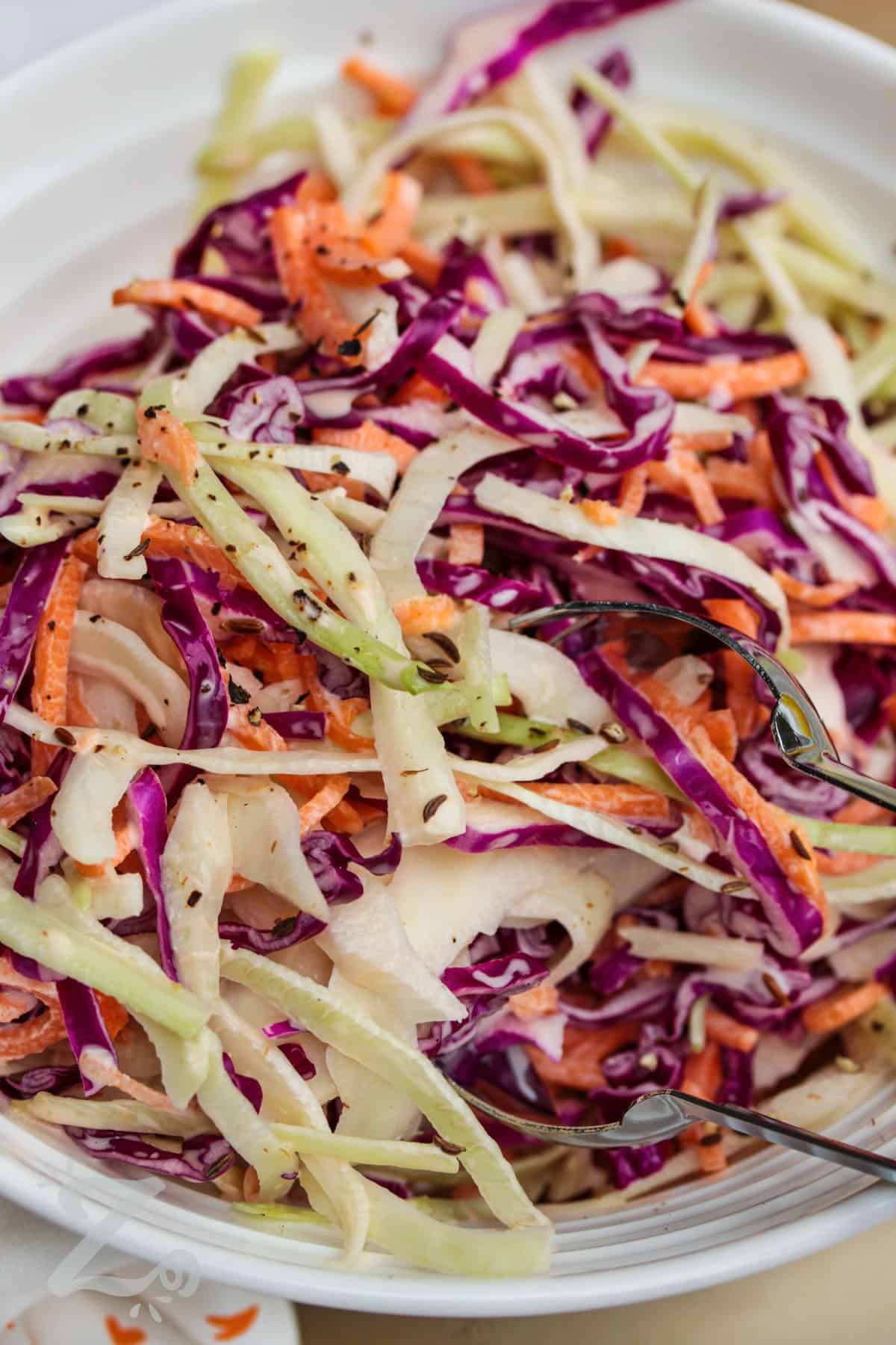 close up of creamy coleslaw in a white bowl with silver tongs