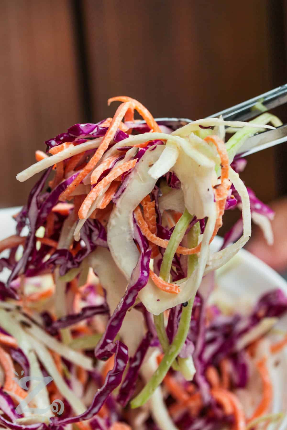 creamy coleslaw being lifted from a bowl with tongs