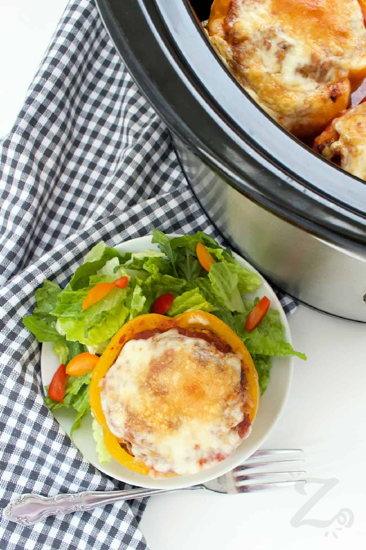 slow cooker stuffed peppers in a crock pot, with one on a white plate with a salad on the side