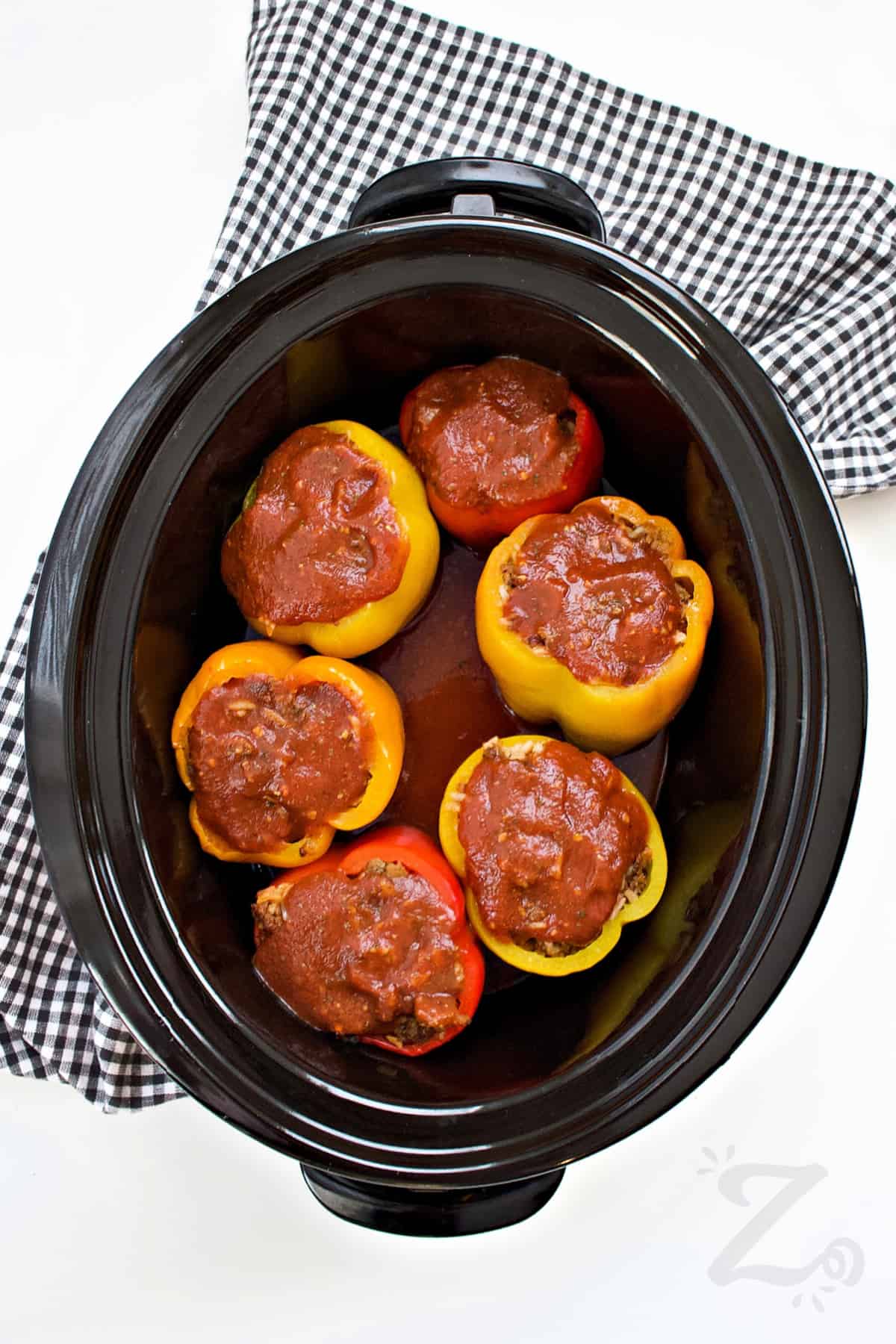 stuffed bell peppers with tomato sauce on top of them in a Crock pot to make slow cooker stuffed peppers