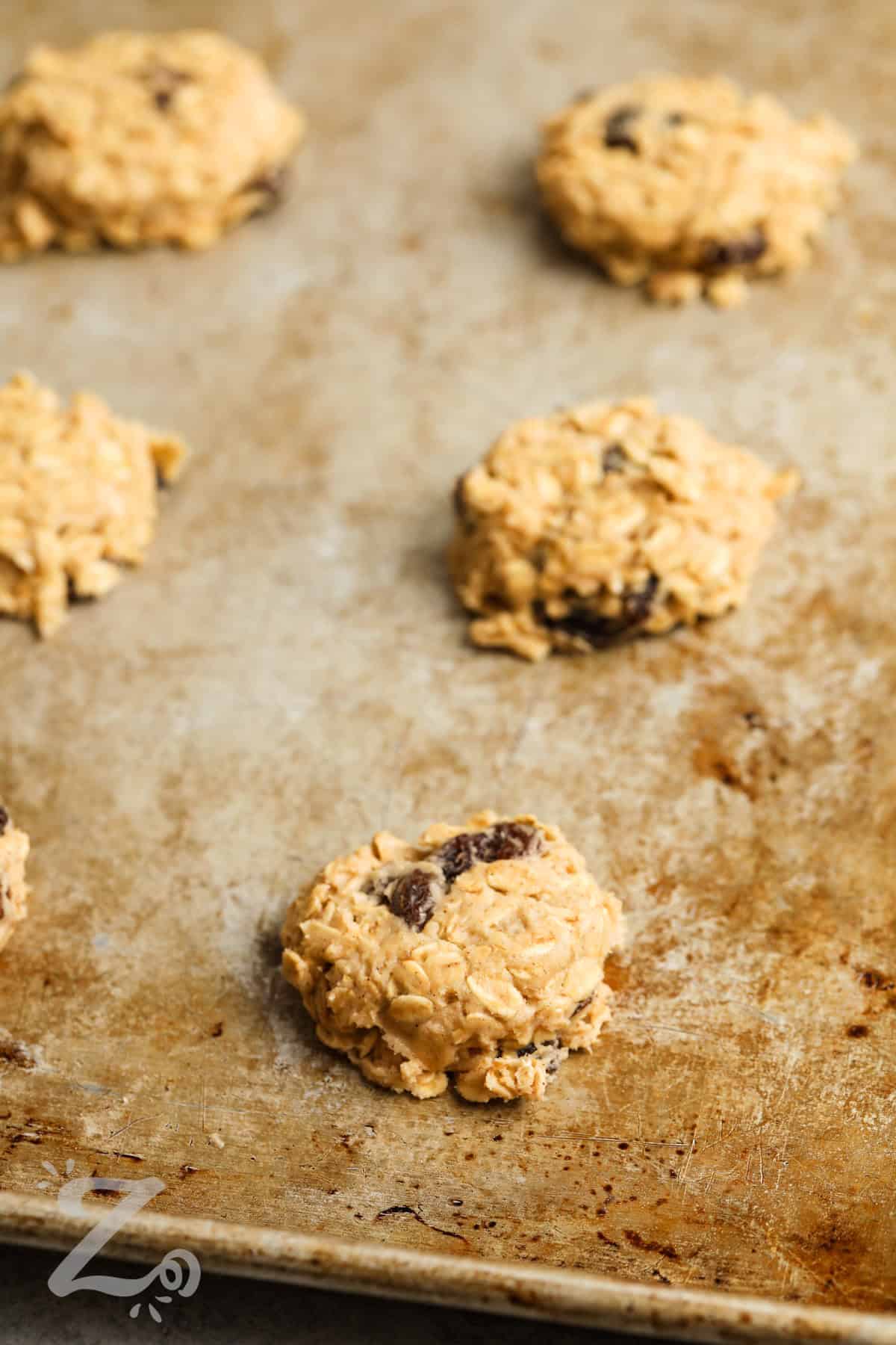 round cookie balls on a sheet pan to make Oatmeal Raisin Cookies