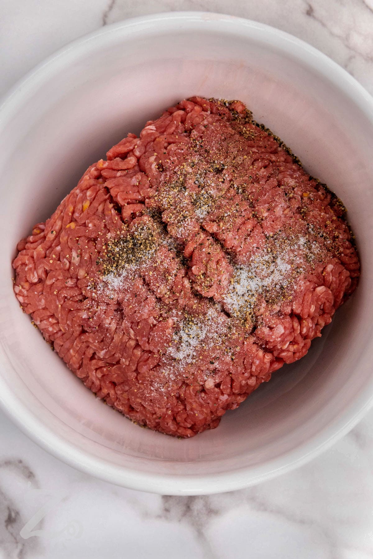 adding seasonings to beef to make Smash Burger Tacos