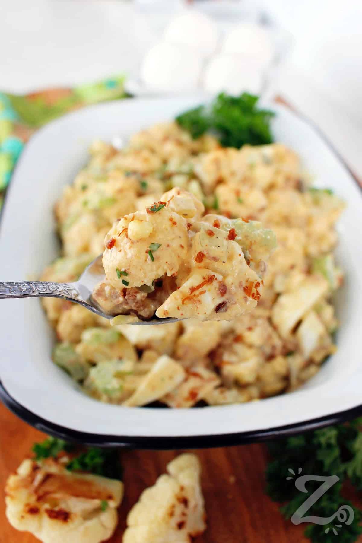 a spoonful of cauliflower potato salad with more in a white rectangular dish in the background