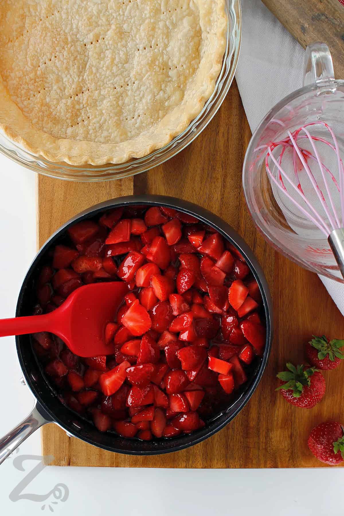 strawberries added to the glaze in a pot, with a baked pie shell on the side, ready to make Fresh Strawberry Pie