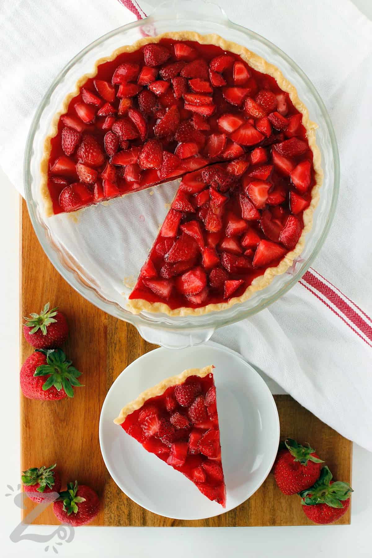 a whole fresh strawberry pie in a clear pie plate with a slice removed and served on a small white plate, with strawberries on the side