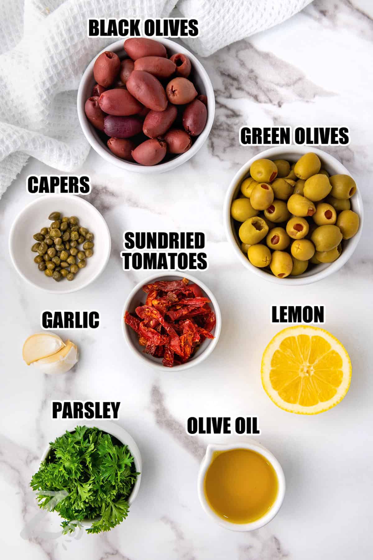 ingredients to make Olive Tapenade including black olives, green olives, capers, sundried tomatoes, lemon, garlic, parsley, olive oil